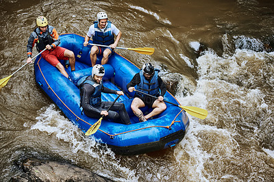 Buy stock photo High angle shot of a group of determined young men on a rubber boat busy paddling on strong river rapids outside during the day