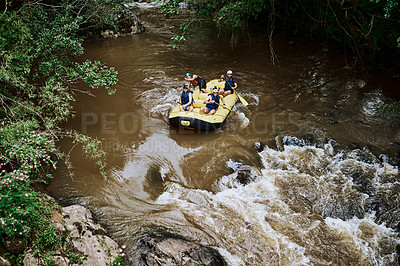 Buy stock photo High angle shot of a group of determined young men on a rubber boat busy paddling on strong river rapids outside during the day
