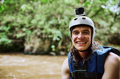 Buy stock photo Portrait of a cheerful young man wearing protective gear and a life jacket while standing next to a river outside during the day