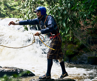 Buy stock photo Shot of a focused middle aged man wearing protective gear while throwing out a rope to somebody in a river outside during the day