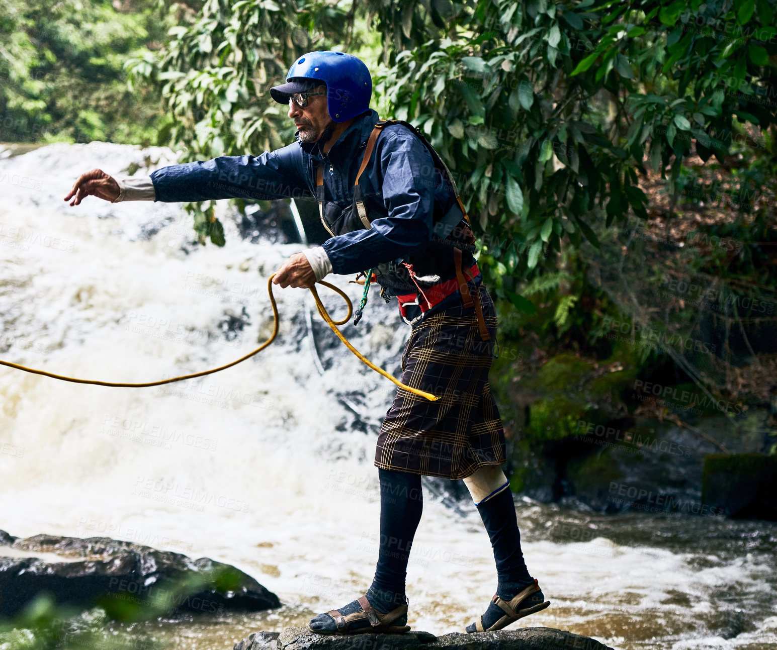 Buy stock photo Shot of a focused middle aged man wearing protective gear while throwing out a rope to somebody in a river outside during the day