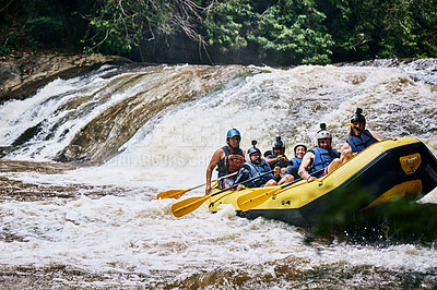 Buy stock photo Shot of a group of determined young people on a rubber boat busy paddling on strong river rapids outside during the day