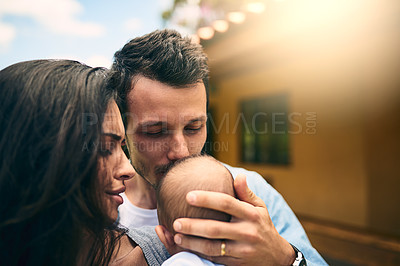 Buy stock photo Cropped shot of a young father kissing his infant son while standing outside with this wife