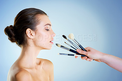 Buy stock photo Studio shot of a hand holding makeup brushes next to a beautiful young woman against a blue background