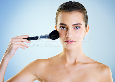 Buy stock photo Studio portrait of a beautiful young woman applying makeup with a brush against a blue background