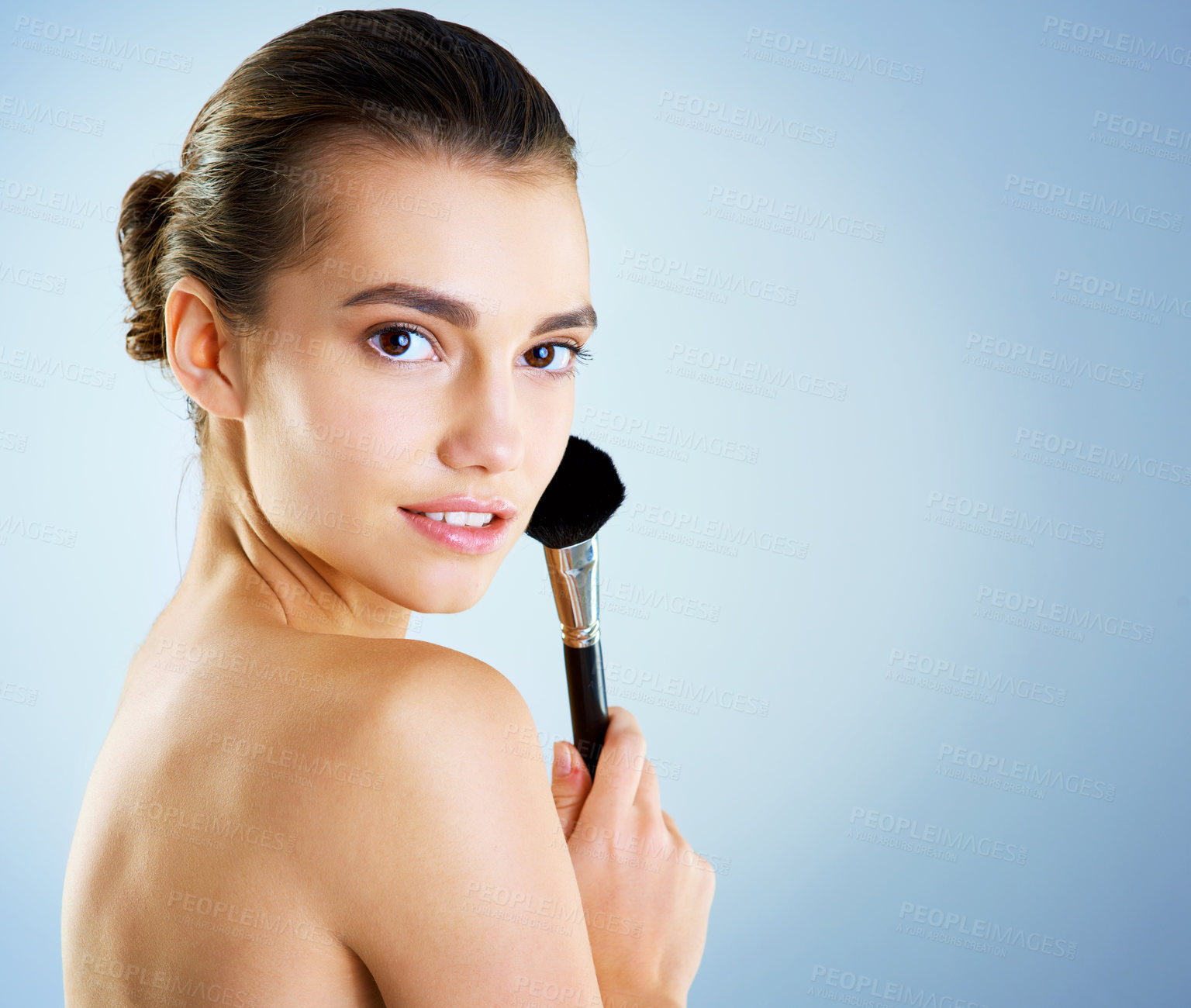 Buy stock photo Studio portrait of a beautiful young woman applying makeup with a brush against a blue background