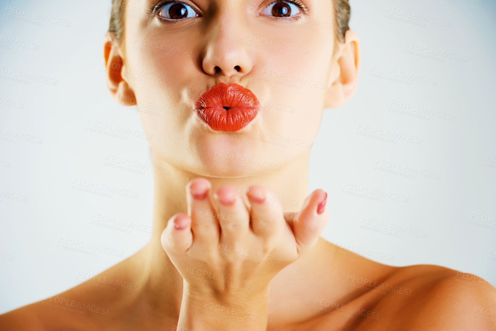 Buy stock photo Cropped studio portrait of a beautiful young woman wearing red lipstick and blowing a kiss against a gray background
