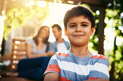 Buy stock photo Portrait of an adorable little boy standing outside with his parents in the background