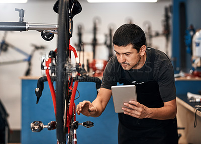 Buy stock photo Shot of a man using a digital tablet in a bicycle repair shop