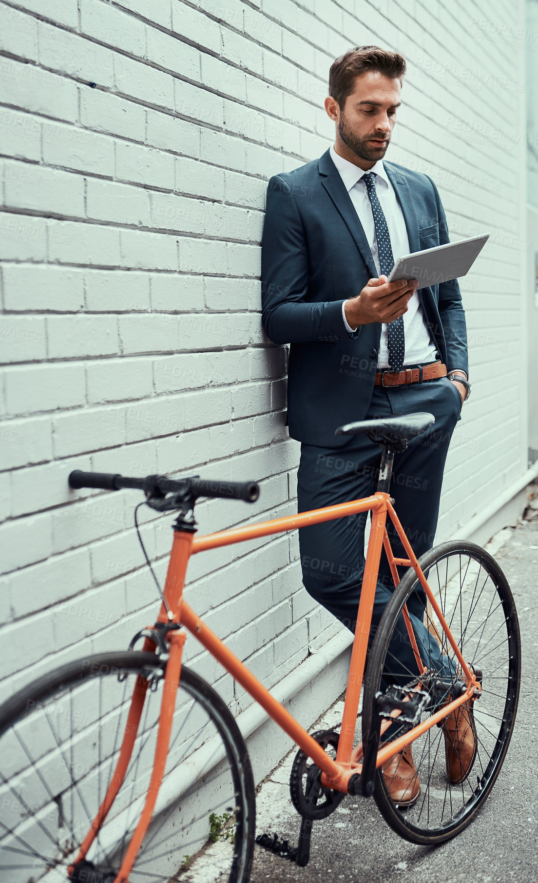 Buy stock photo Shot of a handsome young businessman using a digital tablet while standing alongside his bike outdoors