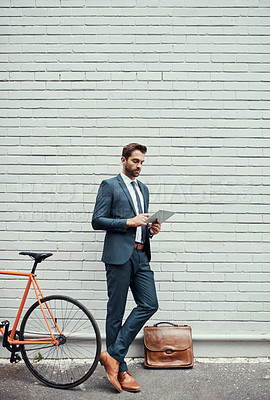 Buy stock photo Business man, tablet and bicycle by wall in city, commute and sustainable travel in metro. Person, suit and bike for eco friendly transportation on digital touchscreen, app and mockup space in Madrid