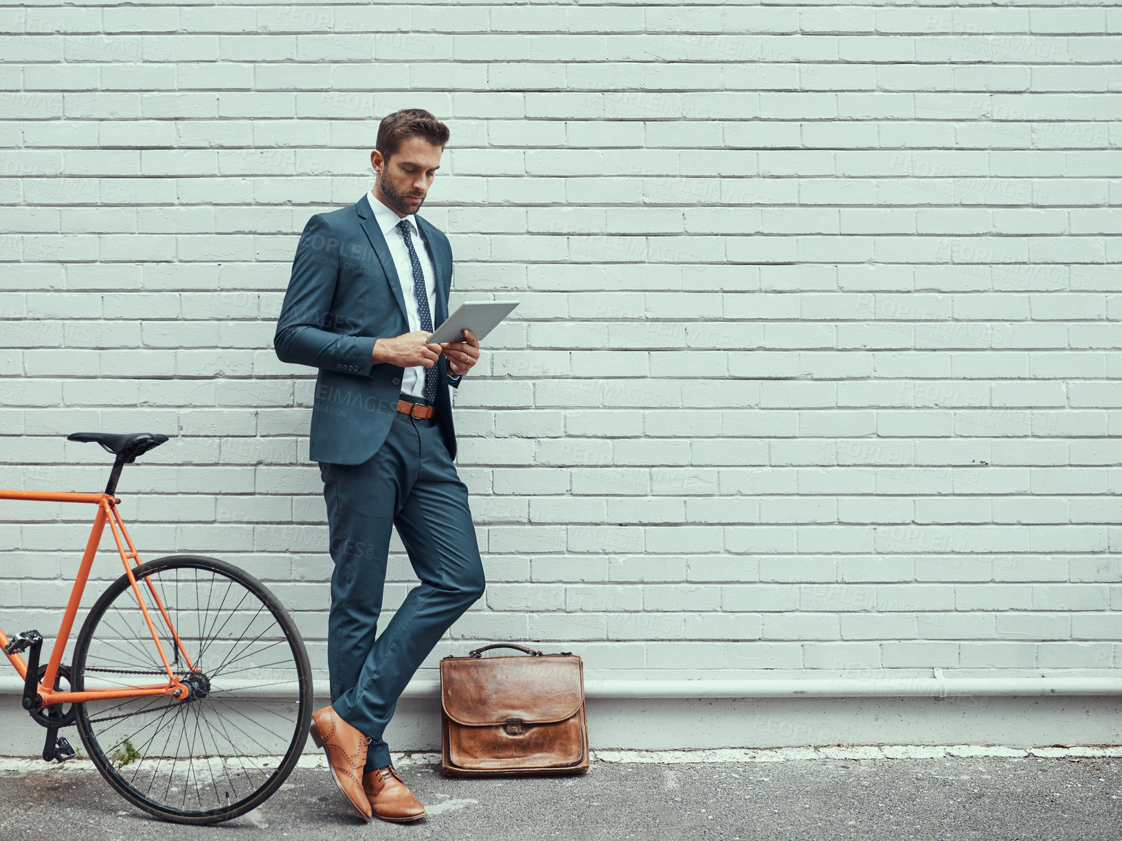 Buy stock photo Shot of a handsome young businessman using a digital tablet while standing alongside his bike outdoors