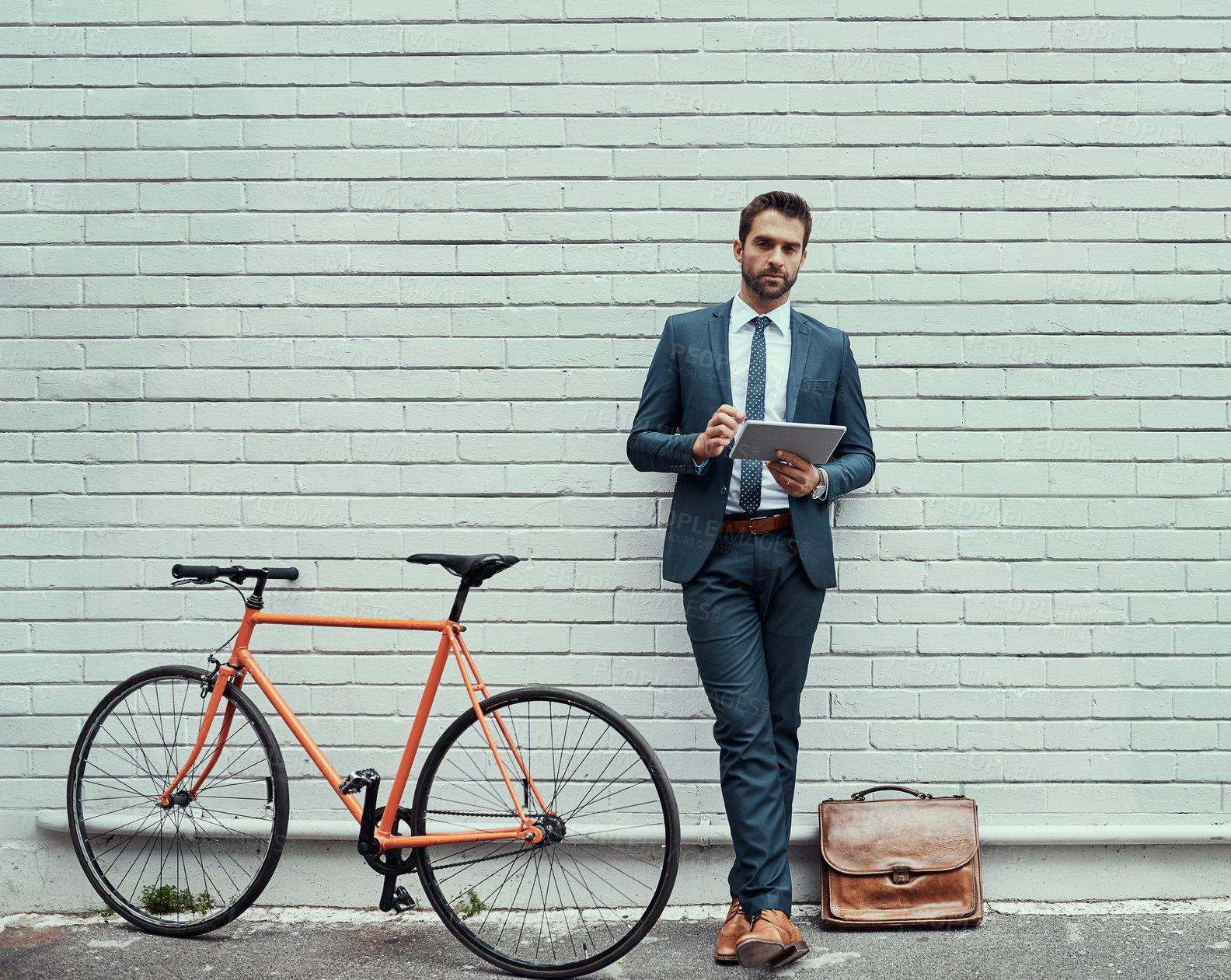 Buy stock photo Portrait of a handsome young businessman using a digital tablet while standing alongside his bike outdoors