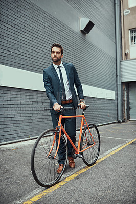 Buy stock photo Shot of a handsome young businessman standing alongside his bike outdoors