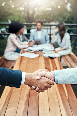 Buy stock photo Closeup shot of two unrecognizable businessmen shaking hands with their colleagues in the background