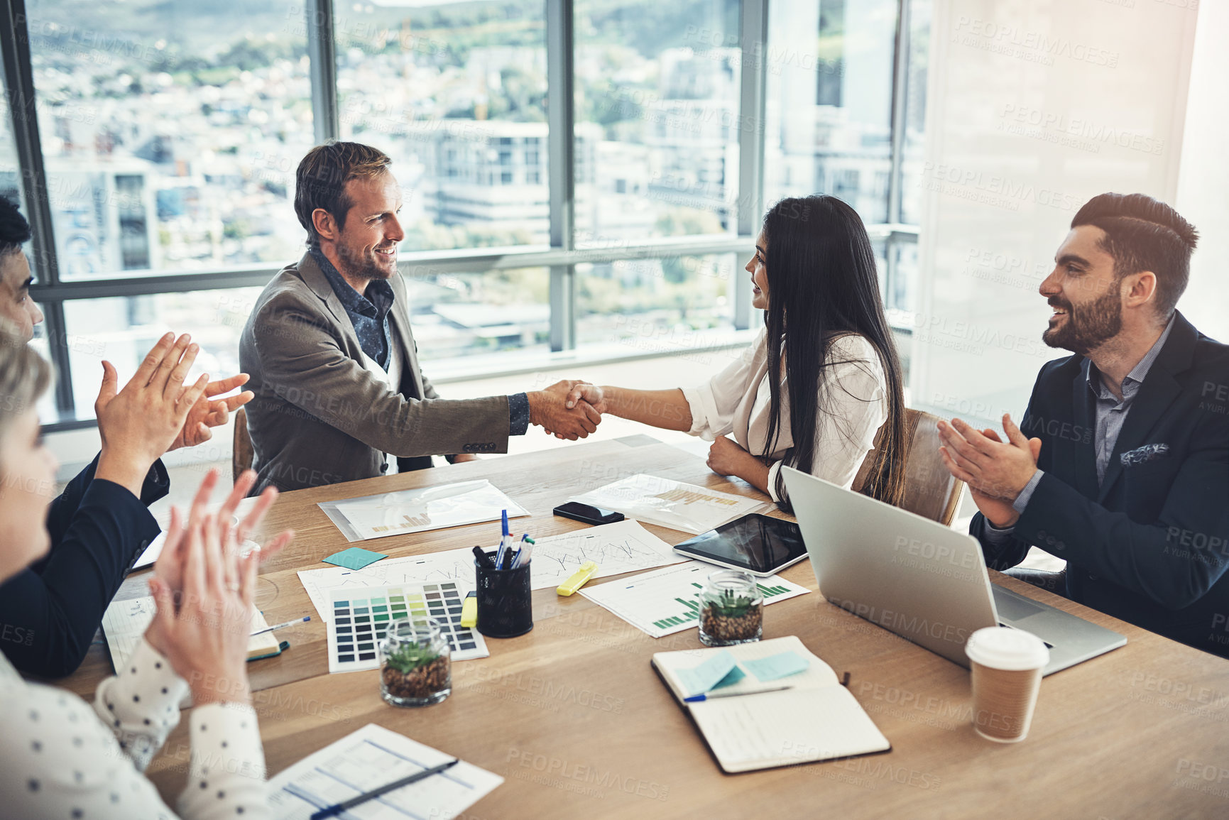 Buy stock photo Shot of two businesspeople shaking hands while their colleagues applaud in an office