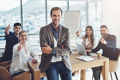 Buy stock photo Portrait of a mature businessman standing in an office with his colleagues showing thumbs up in the background