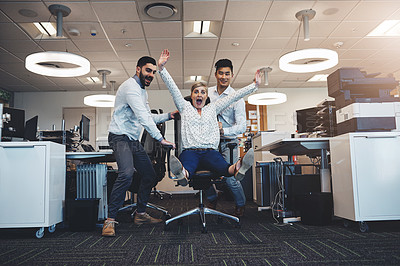 Buy stock photo Shot of businesspeople having fun by taking their colleague for a ride in her chair in the office