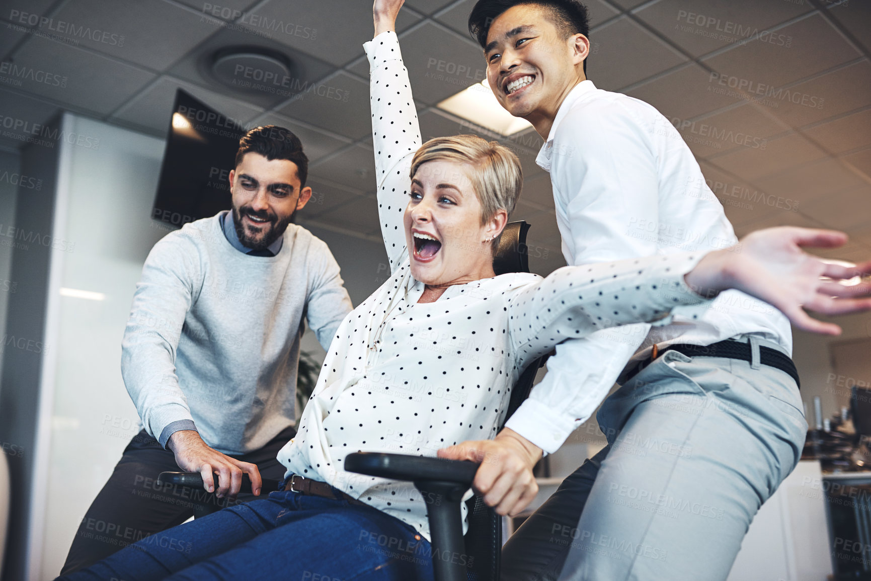 Buy stock photo Shot of businesspeople having fun by pushing taking their colleague for a ride in her chair in the office