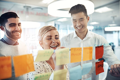 Buy stock photo Shot of businesspeople brainstorming with sticky notes on a glass wall in the office