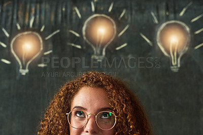Buy stock photo Shot of an attractive young businesswoman standing in front of chalk drawings of lightbulbs on a chalkboard