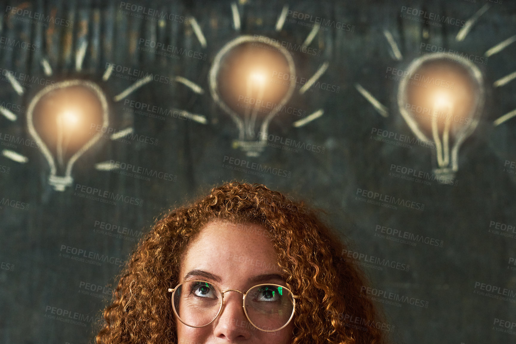 Buy stock photo Shot of an attractive young businesswoman standing in front of chalk drawings of lightbulbs on a chalkboard