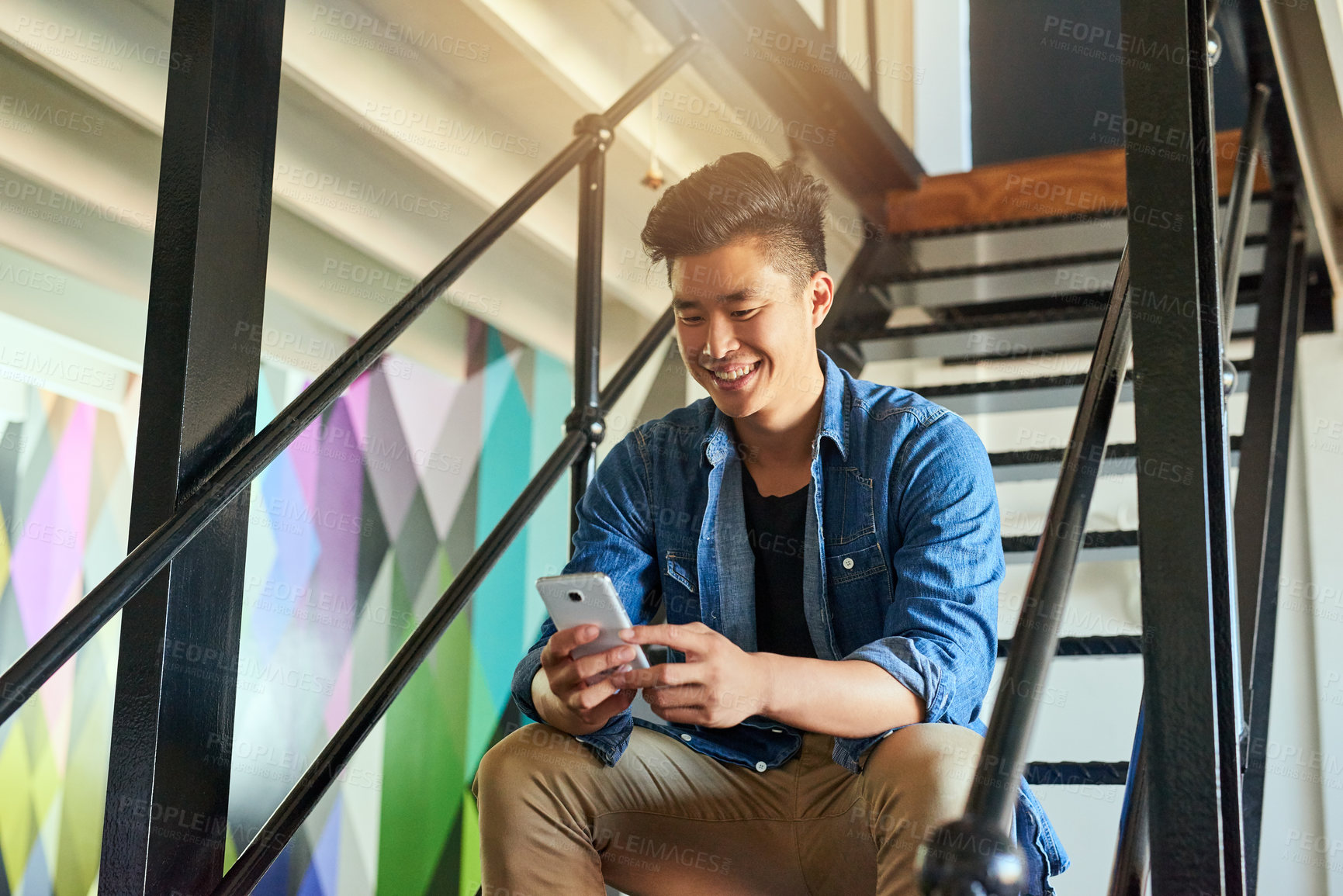 Buy stock photo Asian man, texting and office stairs with smartphone, smile and communication on social network app. Young japanese creative, web design startup and relax on steps in workplace for chat with phone