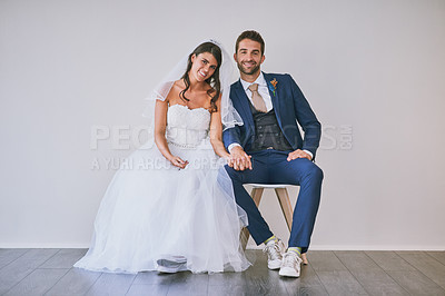 Buy stock photo Studio portrait of a newly married young couple sitting together against a gray background