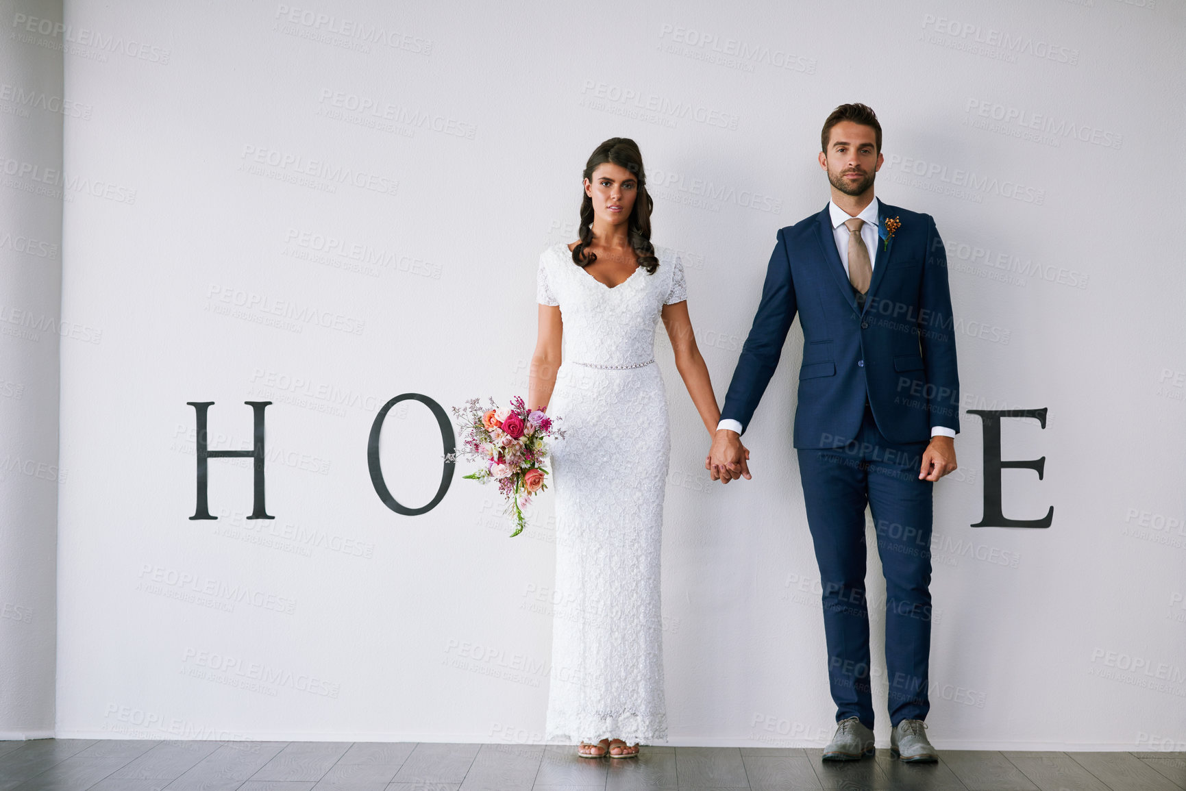 Buy stock photo Concept studio portrait of a bride and groom making an M in the word “home” against a wall