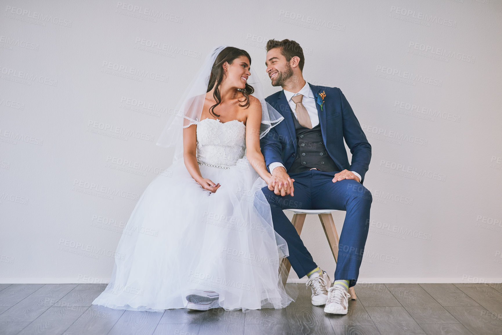 Buy stock photo Studio shot of a newly married young couple sitting together against a gray background