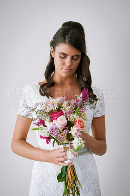 Buy stock photo Studio shot of a young bride holding a bunch of flowers against a gray background