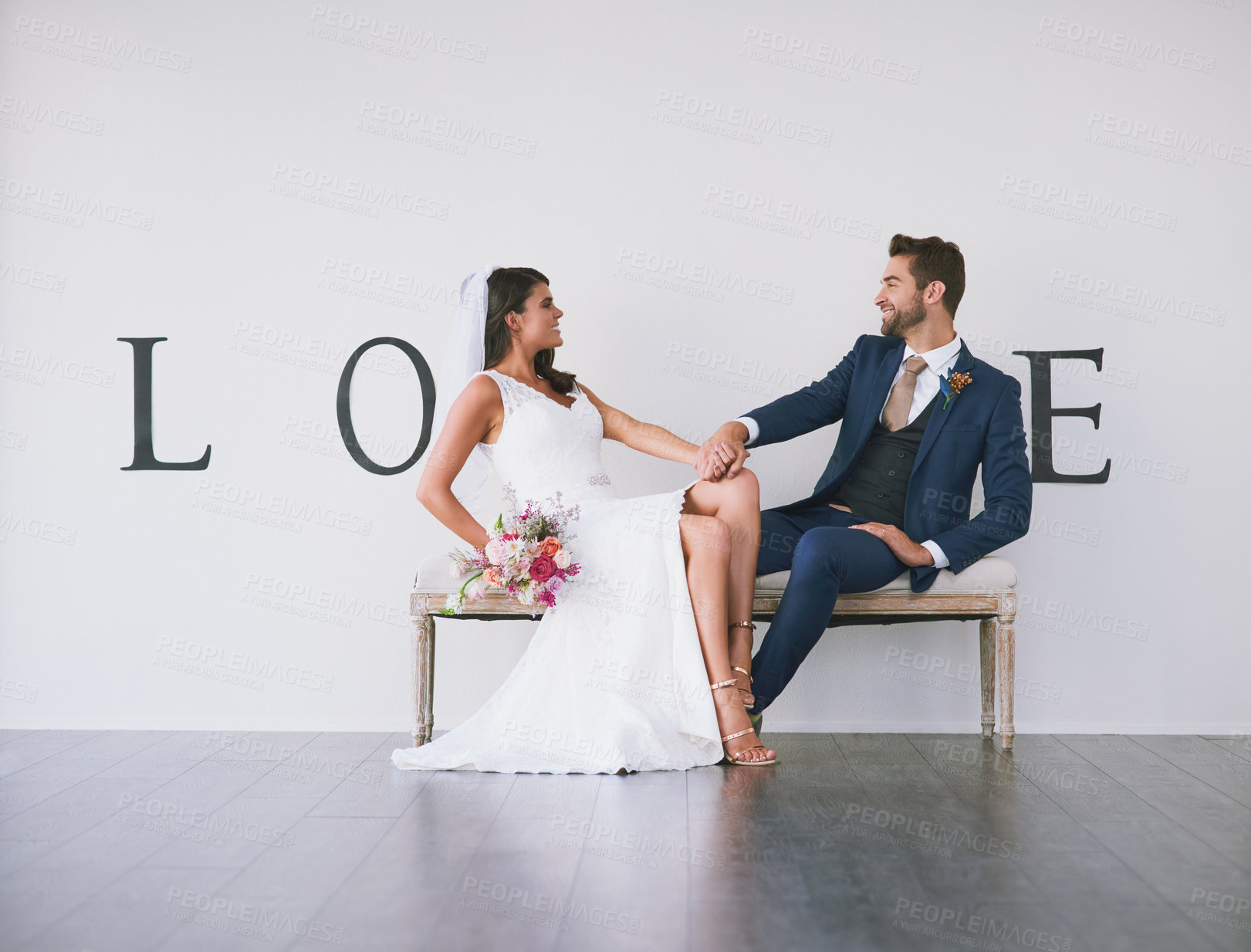 Buy stock photo Concept studio shot of a bride and groom making an V in the word “love” against a wall