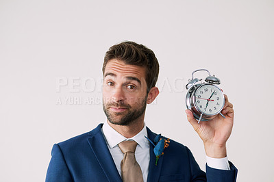 Buy stock photo Studio shot of a handsome young groom holding a clock against a gray background