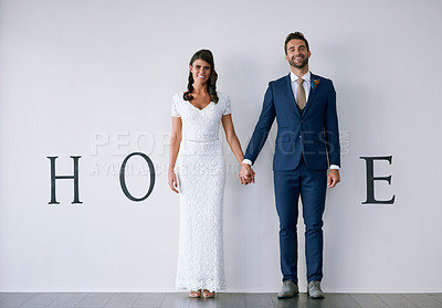 Buy stock photo Concept studio shot of a bride and groom making an M in the word “home” against a wall