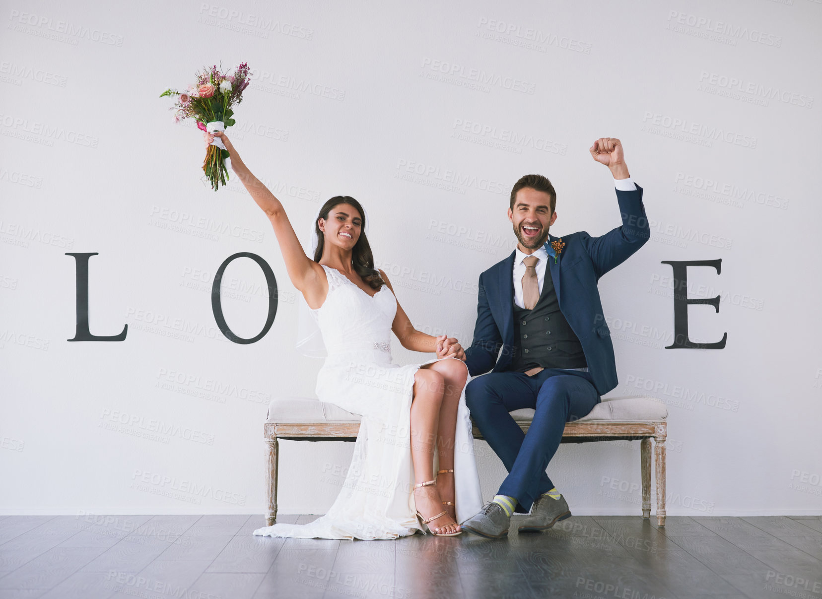 Buy stock photo Concept studio shot of a bride and groom making an V in the word “love” against a wall