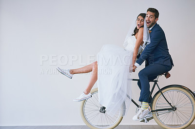 Buy stock photo Studio shot of a newly married young couple riding a bicycle together against a gray background