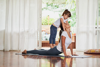 Buy stock photo Shot of a cheerful young woman doing a yoga pose while her young daughter gently stands on her back at home