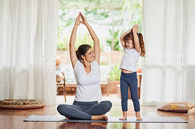 Buy stock photo Shot of a focused young mother and daughter doing a yoga pose together with their arms raised above their heads