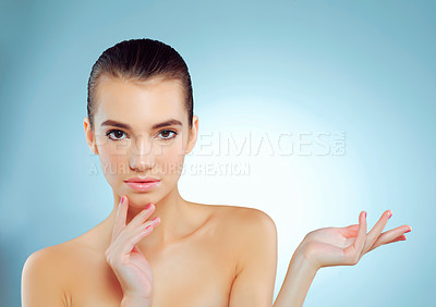 Buy stock photo Studio portrait of a beautiful young woman gesturing towards copy space against a blue background