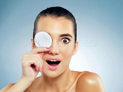 Buy stock photo Studio portrait of a surprised and beautiful young woman covering her eye with a cotton pad against a blue background