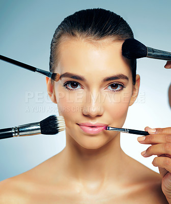 Buy stock photo Studio portrait of hands applying makeup with brushes to a beautiful young woman against a blue background