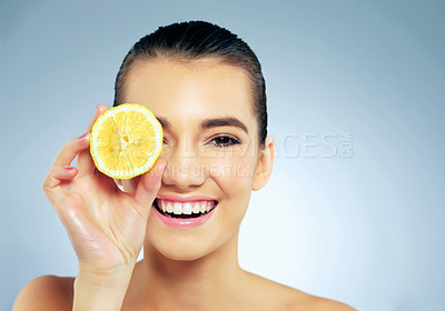 Buy stock photo Studio portrait of a beautiful young woman covering her eye with a lemon against a blue background