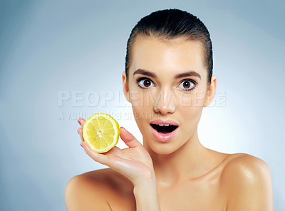 Buy stock photo Studio portrait of a beautiful young woman holding a lemon and looking surprised against a blue background