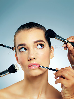 Buy stock photo Studio shot of hands applying makeup with brushes to a beautiful young woman against a blue background