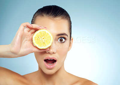 Buy stock photo Studio portrait of a surprised and beautiful young woman covering her eye with a lemon against a blue background