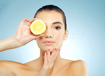 Buy stock photo Studio portrait of a beautiful young woman covering her eye with a lemon against a blue background