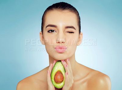 Buy stock photo Studio portrait of a beautiful young woman holding an avocado and blowing a kiss against a blue background