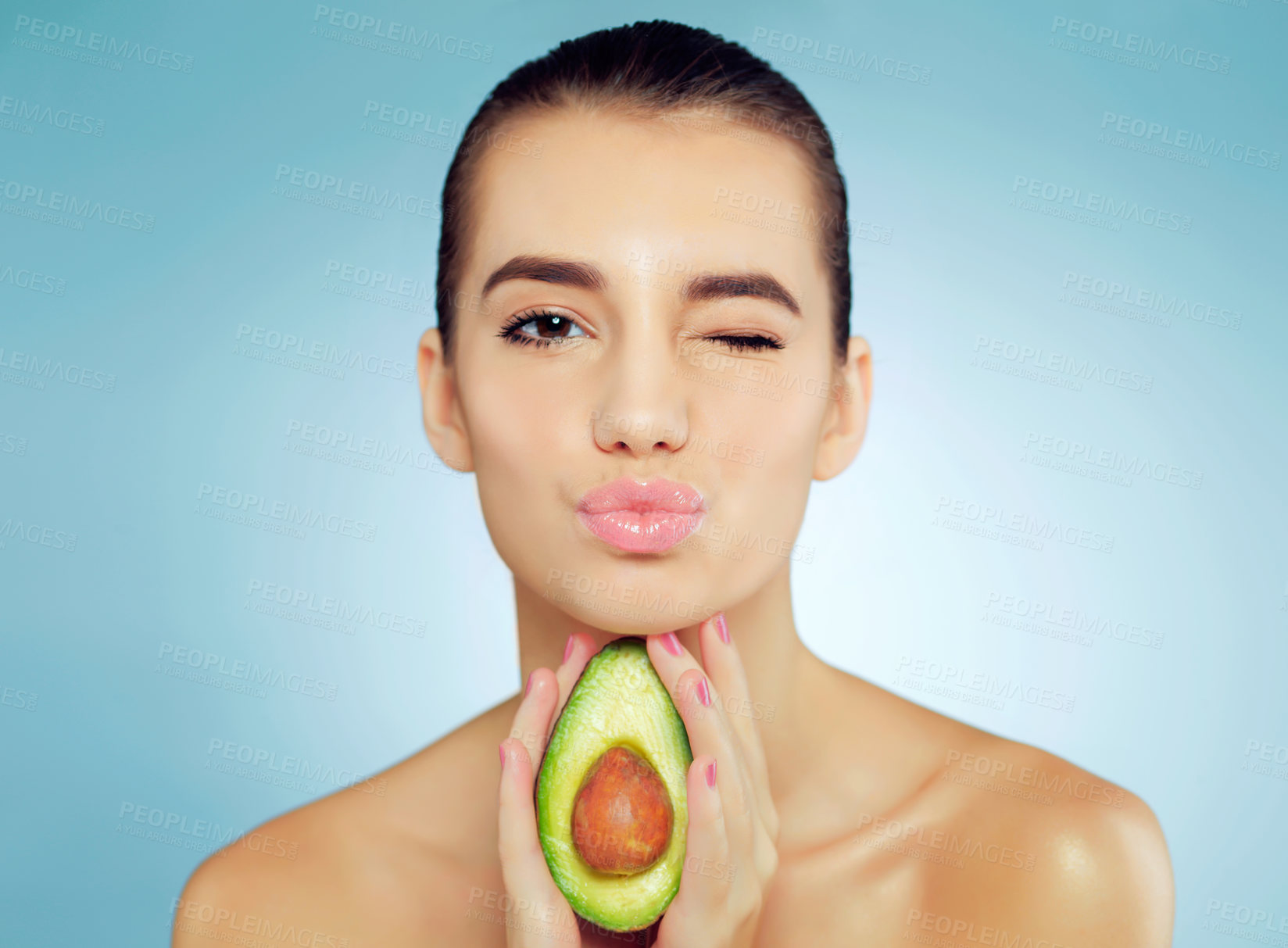 Buy stock photo Avocado, beauty and portrait of woman in studio with natural, organic and face routine with health. Wink, skincare and person with nutrition fruit for facial dermatology glow by blue background.