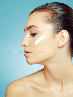 Buy stock photo Studio shot of a beautiful young woman with moisturizer on her cheek against a blue background