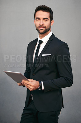 Buy stock photo Studio portrait of a handsome young businessman using a tablet against a grey background